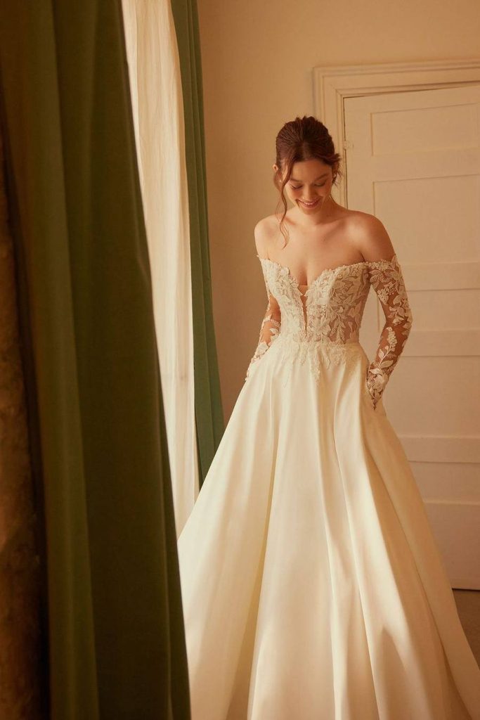 Off-the-shoulder gown with sheer lace long sleeves and a full satin skirt